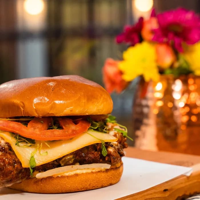 A recent post from The Burgerly’s Instagram — a chef-driven chicken burger plated warm on a live-edge wood board.