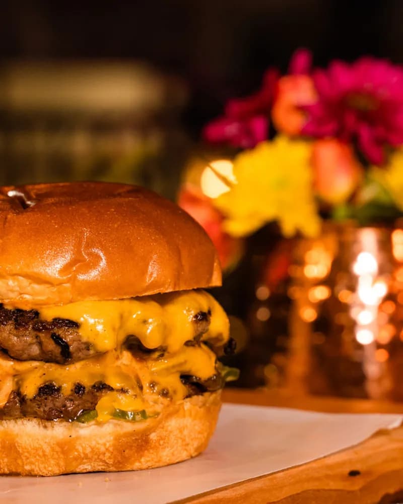 The Burgerly classic cheeseburger with extra sharp American and savory onions on a brioche bun, plated on a live-edge wood board.